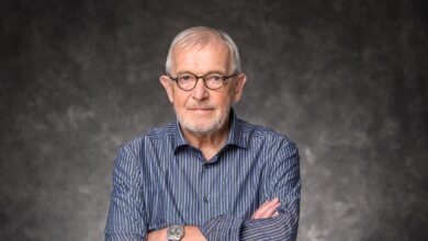 Francis Halzen wearing glasses and a striped shirt, with his arms crossed against a gray background.