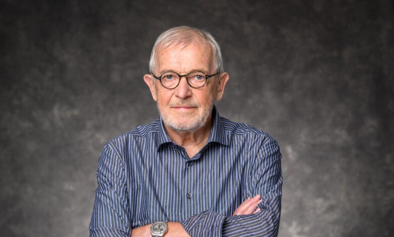 Francis Halzen wearing glasses and a striped shirt, with his arms crossed against a gray background.
