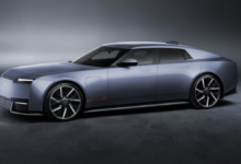 Side profile of the new Jaguar Type 01 electric luxury grand tourer in metallic blue-gray, featuring a long hood, sleek four-door design and large alloy wheels.