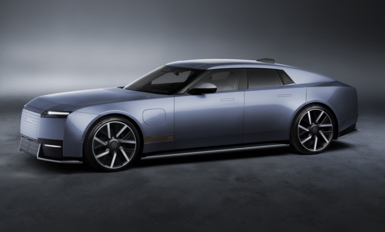 Side profile of the new Jaguar Type 01 electric luxury grand tourer in metallic blue-gray, featuring a long hood, sleek four-door design and large alloy wheels.